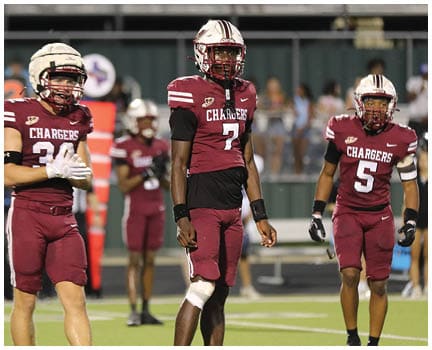 Three people in maroon football uniforms with the word Chargers stand on a field during a game or practice. Description generated by AI
