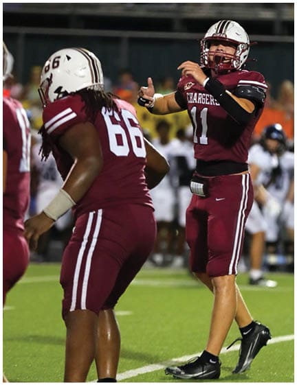Two football players in maroon uniforms and helmets are on the field, with one player preparing to throw a football. Description generated by AI