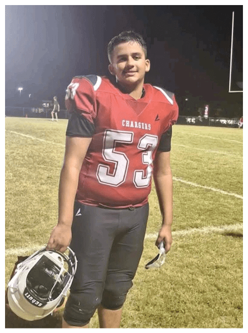 A person wearing a red football jersey with the number 5 is standing on a grassy field at night with another person visible in the background. Description generated by AI