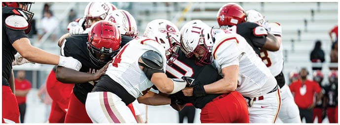 People wearing football helmets and uniforms are engaged in a close physical play on the field. Description generated by AI