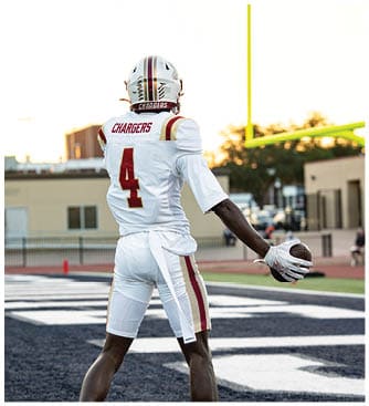 A person wearing a white football helmet and jersey with the word Chargers on the back is standing outdoors against a bright sky. Description generated by AI