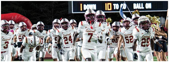 A group of people in football uniforms and cheerleaders are running onto a field with a scoreboard in the background showing the final score of a game at Standridge Stadium. Description generated by AI