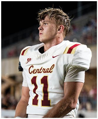 A person wearing a white football uniform with the word Central and the number 11 stands on a field looking to the side. Description generated by AI