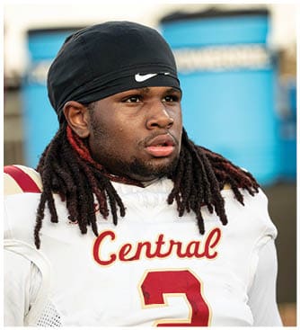 A person with long, thick dreadlocks is wearing a white sports jersey with red and yellow lettering that partially reads “entral" and a large red number. Description generated by AI