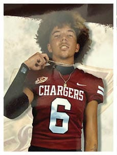 Person with curly hair wearing a maroon football jersey with the word Chargers and number 6, holding a chain necklace. Description generated by AI