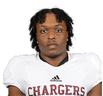 A person with short dreadlocks wearing a white football jersey with the word Chargers and the number 18 on it is looking directly at the camera. Description generated by AI