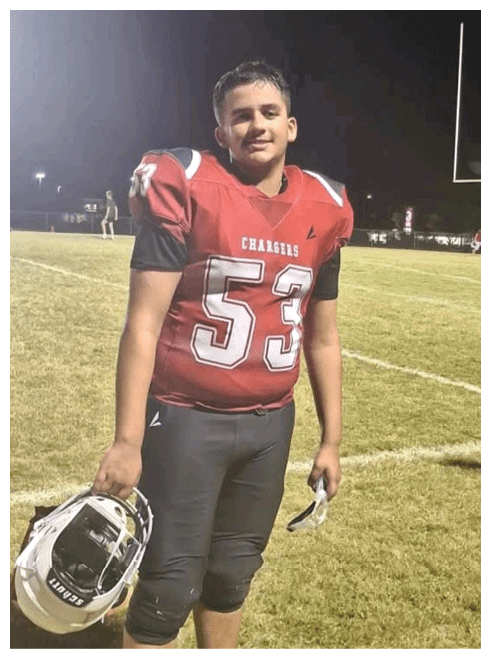 A person wearing a red football jersey with the number 5 is standing on a grassy field at night with another person visible in the background. Description generated by AI