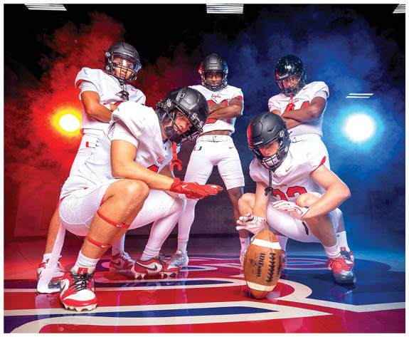 Five people in football uniforms and helmets pose confidently on a colorful indoor court with dramatic red and blue lighting. Description generated by AI