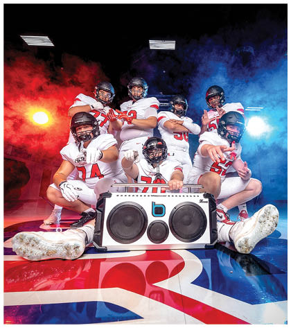 A group of six people wearing white football uniforms and black helmets pose confidently against a background with red and blue smoke. Description generated by AI