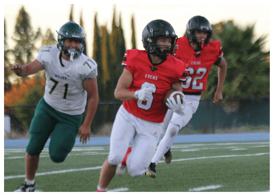 Three people in football uniforms are actively running on a field, with two wearing red jerseys and one in a white jersey. Description generated by AI
