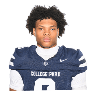 A person with curly hair wearing a navy blue football jersey with the number zero and the words College Park stands facing forward against a plain background. Descripci n generada con IA