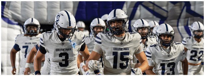 A group of people wearing white football uniforms with helmets are walking together on a field under bright lights. Descripci n generada con IA