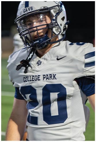A person wearing a white football uniform with “College Park" and the number 80 on the jersey and a white helmet with "GAVS" on it is on a dark field. Descripci n generada con IA