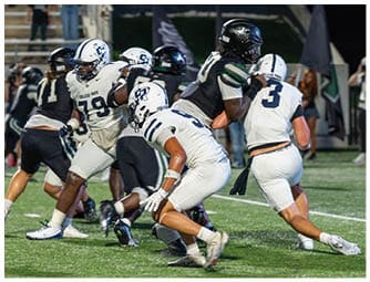 People wearing football uniforms are actively engaged in a play on a well-lit field during a game. Descripci n generada con IA