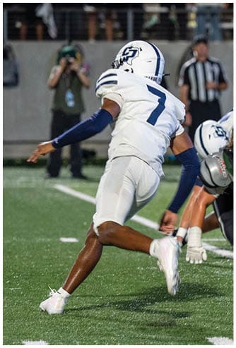 Several people in football uniforms are engaged in a close, intense play on a grassy field under bright lighting. Descripci n generada con IA