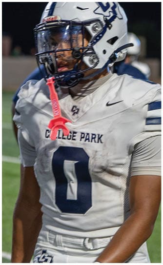 A person wearing a white football uniform with the number zero and a helmet stands on a field at night. Descripci n generada con IA