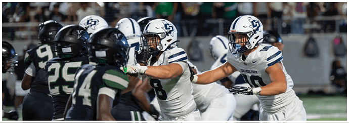 People in sports uniforms are engaged in a football game on a grassy field with some players running and others preparing to block. Descripci n generada con IA