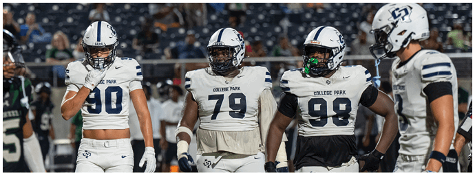 Four people wearing football uniforms with helmets and shoulder pads stand together on a field during a game. Descripci n generada con IA