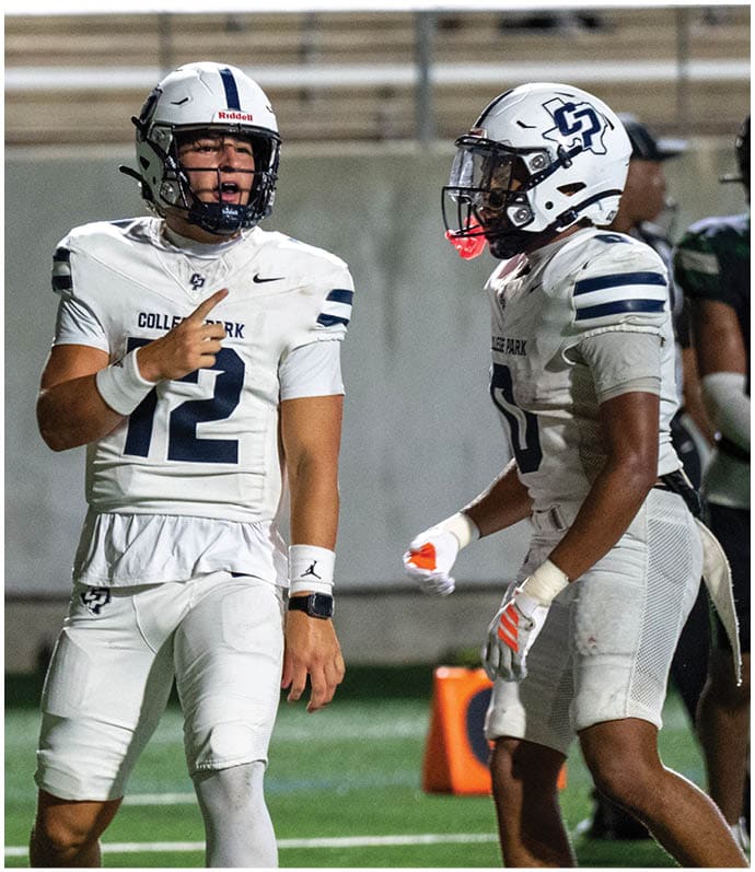 Two football players in white uniforms and helmets are on a field with one pointing while the other listens during a game. Descripci n generada con IA