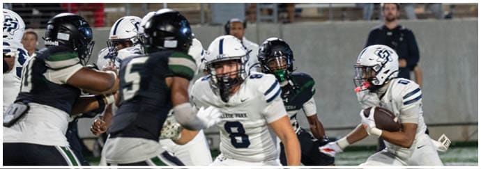 People in football uniforms are actively engaged in a game on a field with one person holding the ball and others preparing to block or tackle. Descripci n generada con IA