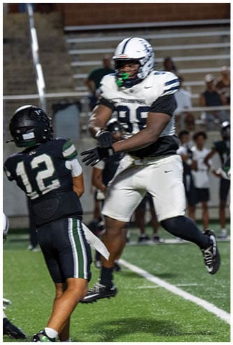A person wearing a black football uniform with the number 12 is preparing to throw a football while two other players in white and black uniforms are nearby on a green field. Descripci n generada con IA