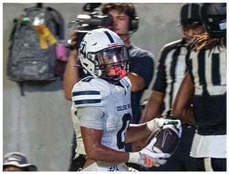 Two people in football uniforms are on the field near a referee while several people in casual clothing watch from the bleachers behind them. Descripci n generada con IA