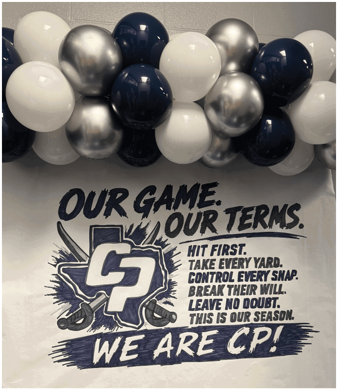 A decorative balloon arch in white, silver, and dark blue hangs above a wall with bold text reading “OUR GAME. OUR TERM." alongside a stylized logo and motivational phrases about hitting first, taking every yard, and controlling every snap. Descripci n generada con IA