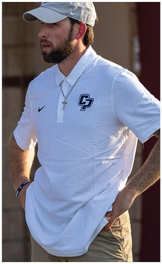 A person wearing a light-colored cap and a white polo shirt with a “CP" logo and a cross necklace is looking to the side in an outdoor setting. Descripci n generada con IA