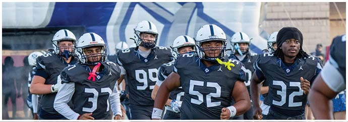 A group of people wearing football uniforms and helmets are running onto a field from a tunnel. Descripci n generada con IA