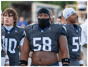 Three people wearing dark football uniforms with numbers and standing closely together, with one person in the center wearing a head covering and wristbands. Descripci n generada con IA