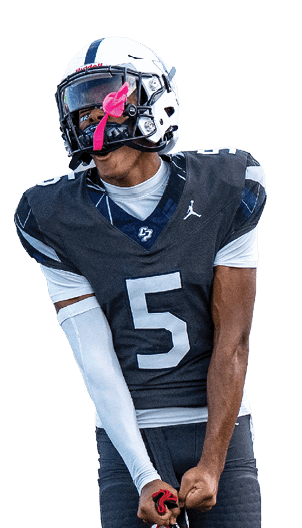A person wearing a dark football uniform with the number five is standing on a field holding a football. Descripci n generada con IA