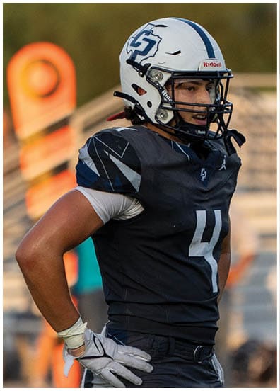 A person wearing a football uniform with the number 4 and a white helmet stands on a field with hands on hips. Descripci n generada con IA