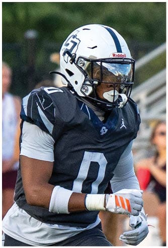 A person wearing a black and white football uniform and helmet is standing outdoors with a blurred background. Descripci n generada con IA