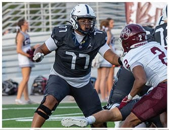 Two people in football uniforms are engaged in a play on a green field with white yard lines, with one person wearing a black uniform and the other wearing a white and maroon uniform. Descripci n generada con IA