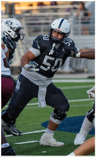 A person wearing a black and white football uniform with the number 50 is actively engaged in a play on a football field with other players around. Descripci n generada con IA