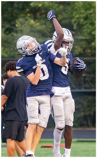 A person wearing a black football helmet and a white Bishop Verot jersey with the number 17 is raising their arms. Descripci n generada con IA