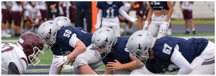 People wearing green and white football uniforms are actively engaged in a play on a football field. Descripci n generada con IA