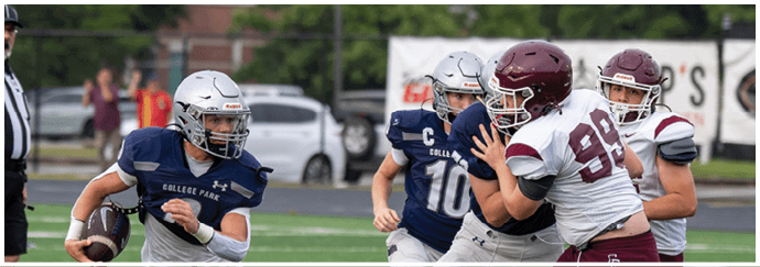 Four people in football uniforms are running on a field with one person in a green uniform holding a football and three others in white uniforms chasing behind. Descripci n generada con IA