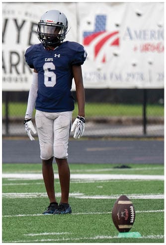 A person wearing a football uniform with the number 15 is running on a field while holding a football. Descripci n generada con IA