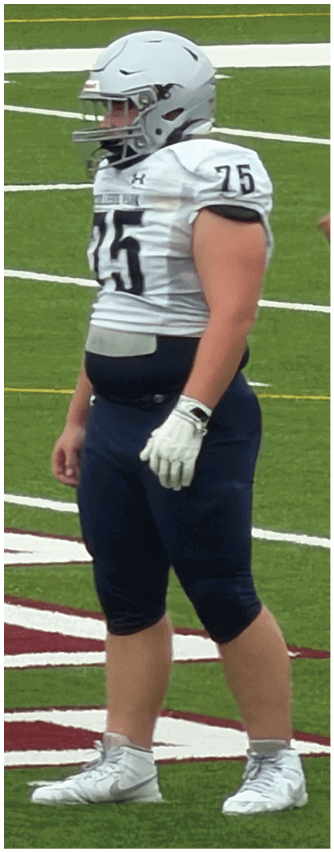 A person wearing a white and black football uniform with the number 20 and the words Bishop Verot is standing on a field with a pink mouthguard hanging from their helmet. Descripci n generada con IA
