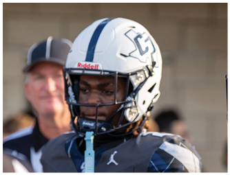 A person wearing a white football helmet with a blue stripe and a logo on the side is shown in close-up. Descripci n generada con IA