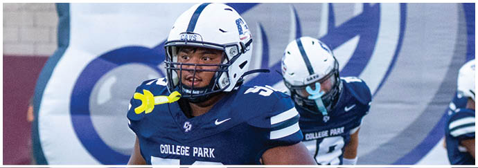 Two people wearing white football helmets and uniforms are standing in front of a large blue and white banner. Descripci n generada con IA