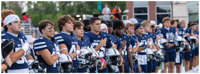 A line of people wearing matching sports uniforms stand side by side holding helmets, appearing to participate in a pre-game ceremony on a field. Descripci n generada con IA