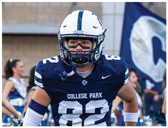 A person wearing a white football helmet and navy blue jersey with the number 88 is on a field with a blurred flag in the background. Descripci n generada con IA