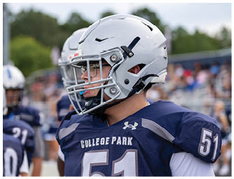 An adult wearing a backward cap adjusts the helmet of a person in a football uniform with the number seven on it during a practice or game. Descripci n generada con IA