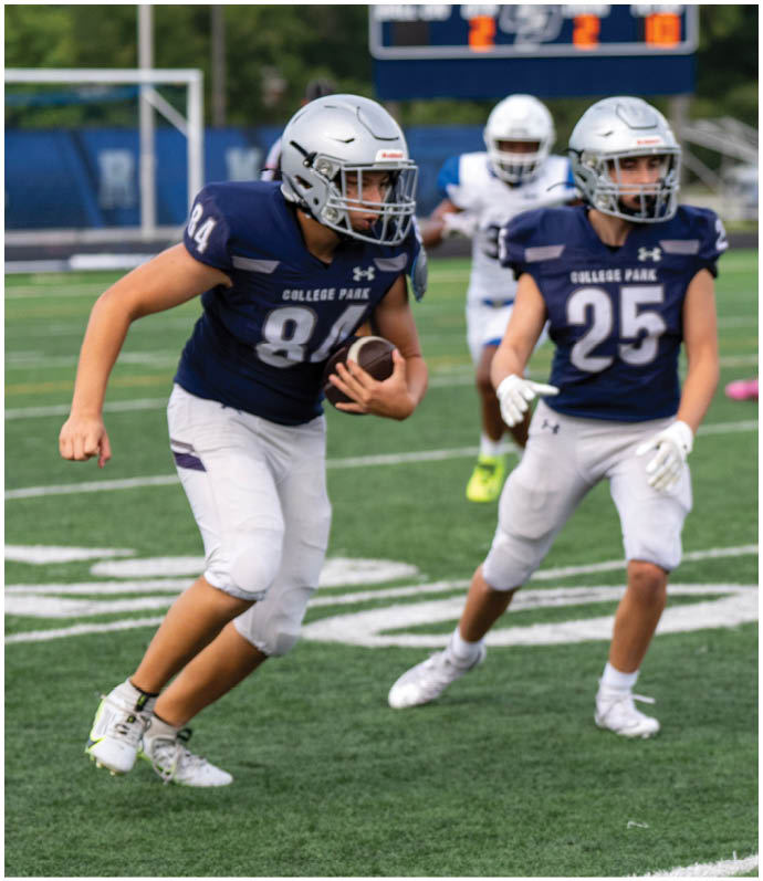 Three people wearing white football uniforms with helmets walk together on a green field during a game or practice. Descripci n generada con IA