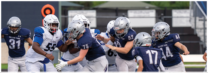 People wearing green and white football uniforms are actively engaged in a play on a football field. Descripci n generada con IA