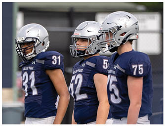 Three people in football uniforms with helmets are actively engaged in a game on a field with others in the background. Descripci n generada con IA