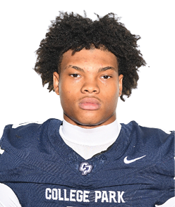 A person with curly hair wearing a navy blue football jersey with the number zero and the words College Park stands facing forward against a plain background. Descripci n generada con IA