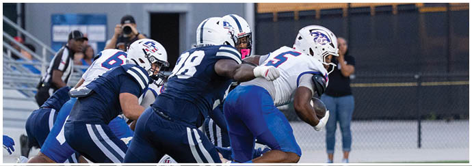 People in football uniforms are engaged in a play on a field with one person running while others attempt to block or tackle. Descripci n generada con IA